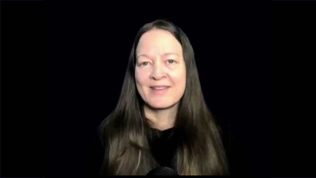 Photograph of Yvette Marks, smiling, with long dark hair and a black background