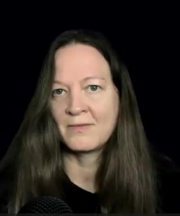 Photograph of Yvette Marks, smiling, with long dark hair and a black background